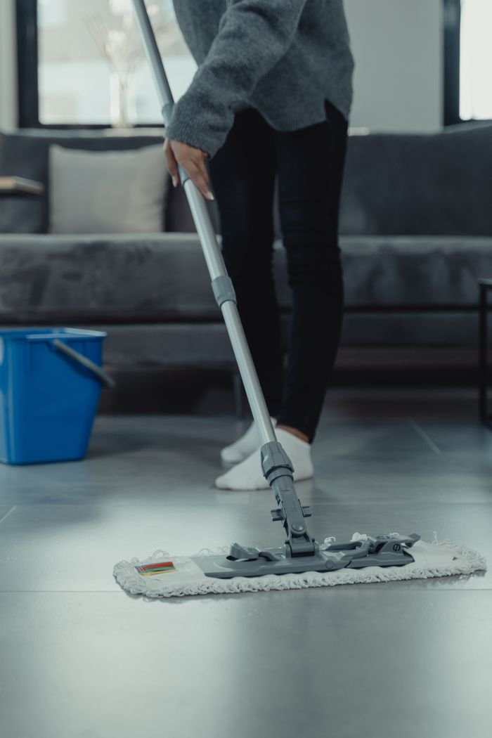 End of Tenancy Cleaning Close-up of person mopping a clean tile floor in a contemporary living room.